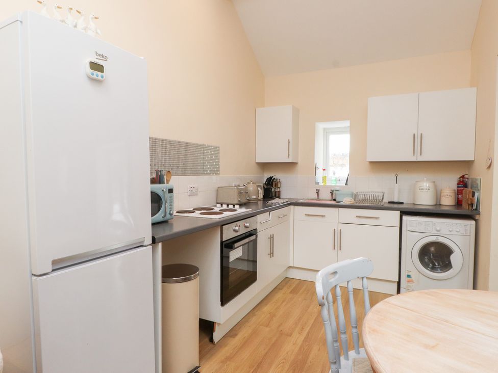 A kitchen with white cabinets and appliances at Swallow Cottage in Llangefni