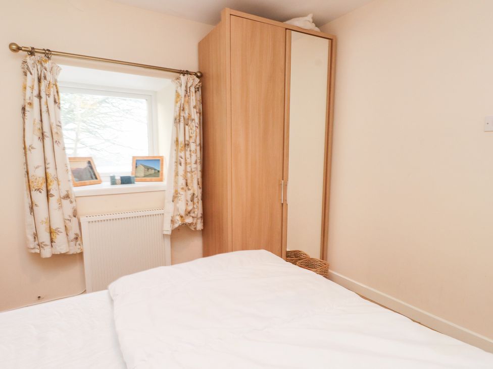 A bedroom with a bed, wardrobe, window, and radiator at Swallow Cottage in Llangefni