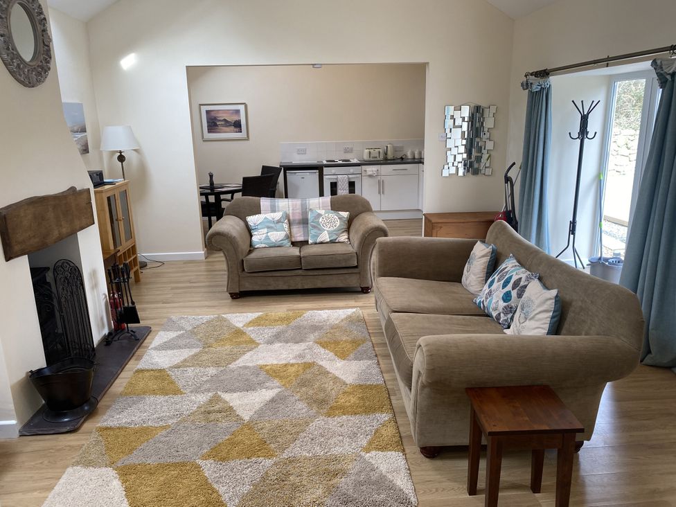 A living room with sofas and kitchen area at Swallow Cottage in Llangefni