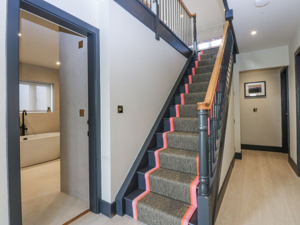 A hallway with stairs leading up and a bathroom door at Bell House in Llanfechell