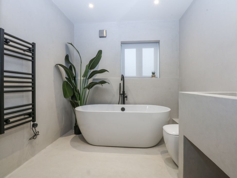 A bathroom with a bathtub, toilet and a towel warmer at Bell House in Llanfechell