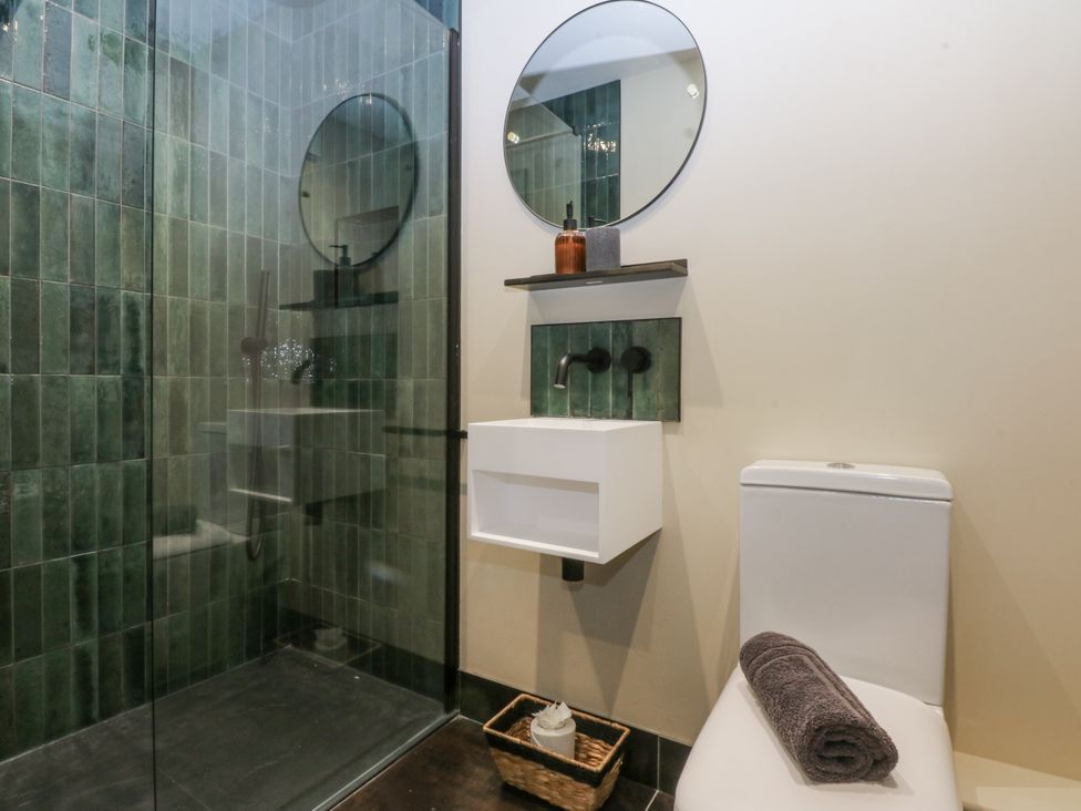 A bathroom with a shower, sink, toilet, and mirror at Bell House in Llanfechell