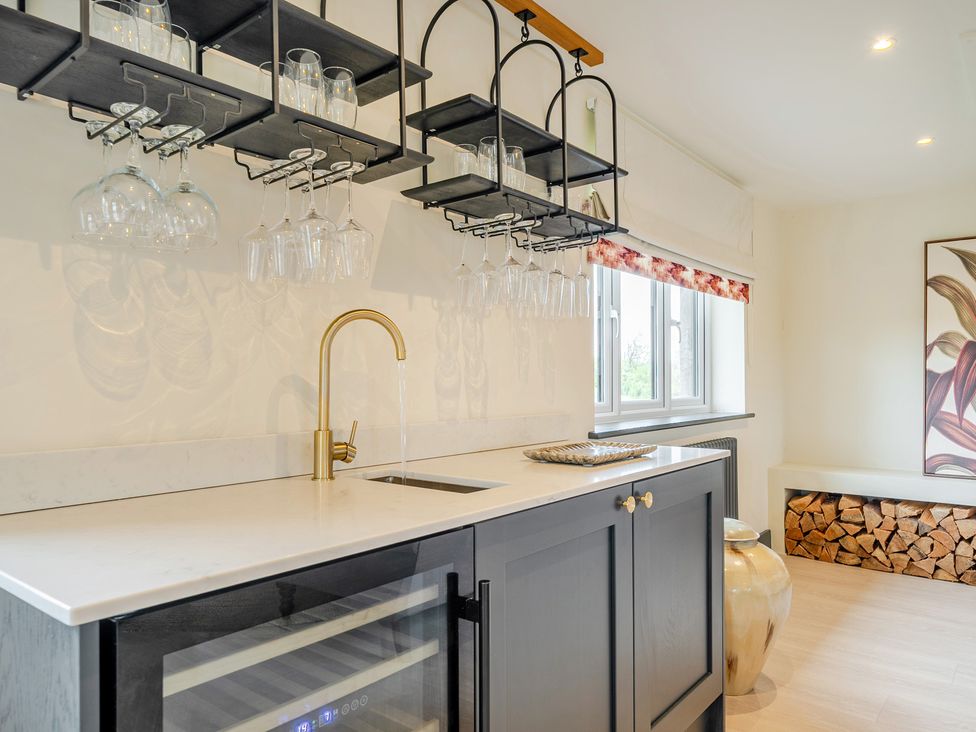 A kitchen with a sink, wine cooler and shelves holding glasses at Bell House Llanfechell