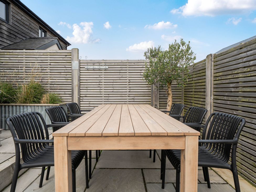 An outdoor dining area with a wooden table and black chairs at Bell House in Llanfechell
