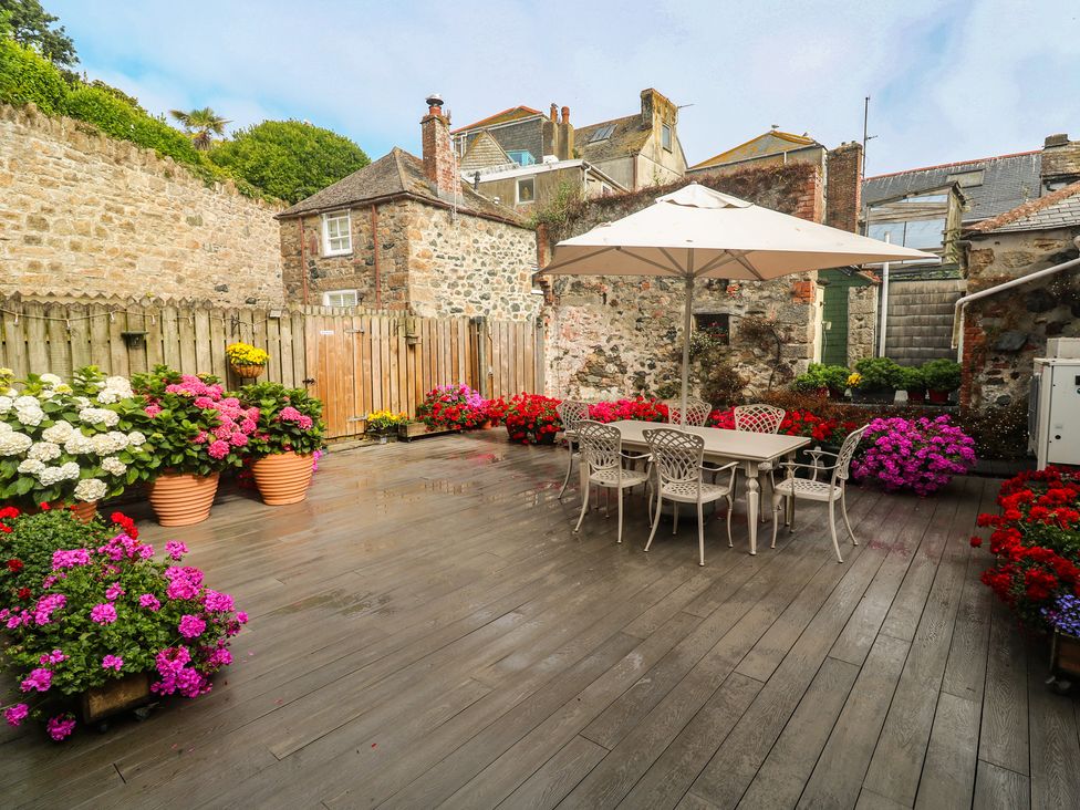 A garden with flower pots and a dining table under an umbrella at Ammil Bespoke in St Ives