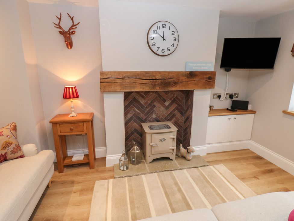 A living room with a clock, television, and fireplace at Brooklyn Cottage in Kirkby Malzeard