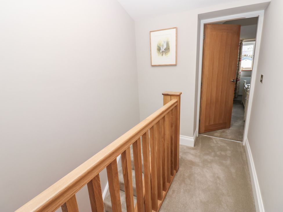 A hallway with a stair railing and door at Brooklyn Cottage in Kirkby Malzeard