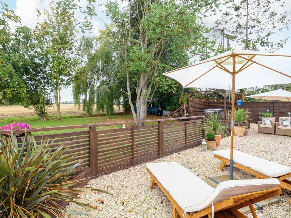 A garden with sun loungers and a parasol at Three Ways South Lopham near Garboldisham