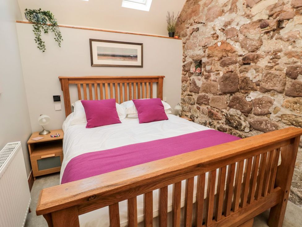 A bedroom with a bed and stone wall at Cygnet Cottage in Berwick-upon-Tweed