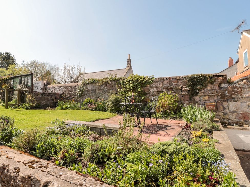A garden with a table and chairs surrounded by flowers at Cygnet Cottage in Berwick-upon-Tweed