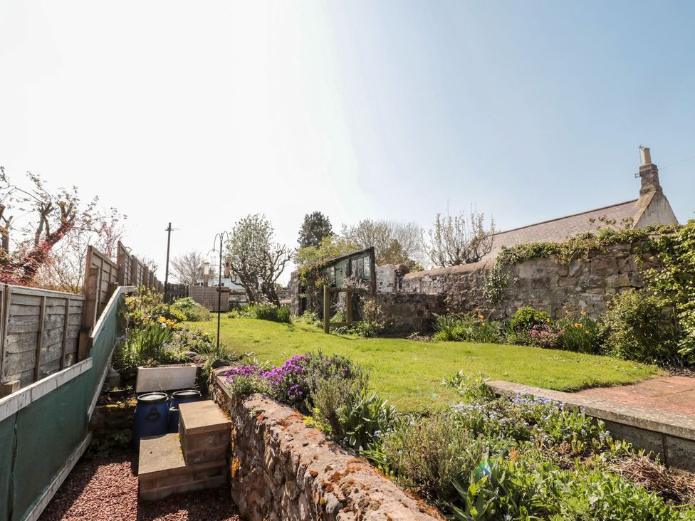 A garden with grass, plants, and a stone wall at Cygnet Cottage in Berwick-upon-Tweed