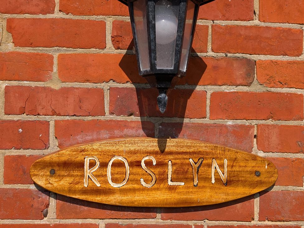 A wooden sign reading ROSLYN next to a lamp on a brick wall at Roslyn in Romsey