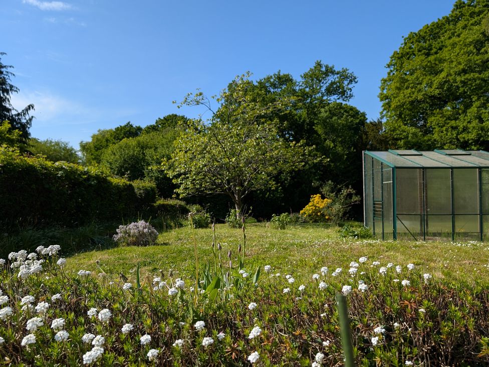 A garden with a greenhouse and flower beds at Roslyn in Romsey