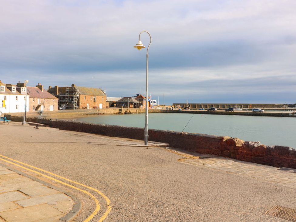 A harbor with buildings and vehicles near the water at The Harbour Hoose Stonehaven