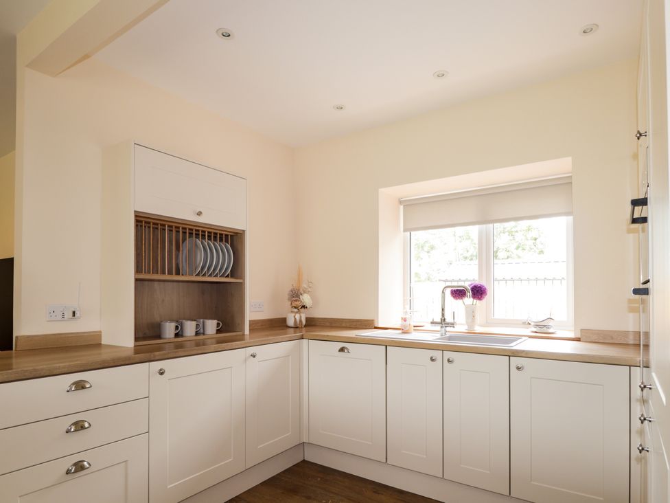 A kitchen with a sink, window, and plates in a cupboard at Millmoss Cottage