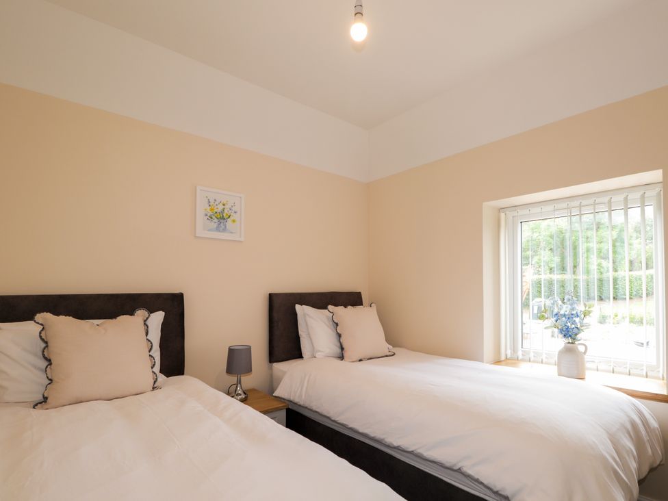 A bedroom with two beds and a window at Millmoss Cottage