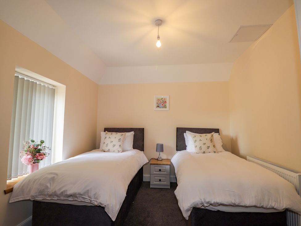 A bedroom with two beds and a window at Millmoss Cottage