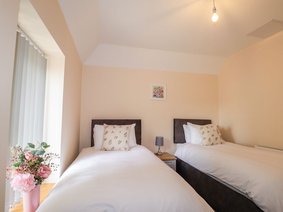 A bedroom with two beds and a flower arrangement at Millmoss Cottage 