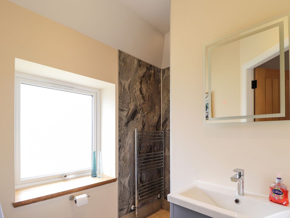 A bathroom with a window, sink, mirror, and heated towel rail at Millmoss Cottage 