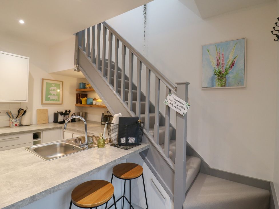 A kitchen with a staircase, bar stools, and wall art at The Kiln in Colmworth