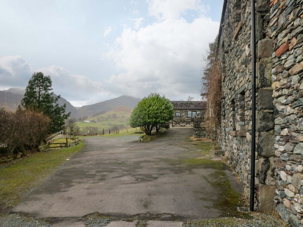 An outdoor view of a stone building with trees and mountains at Newlands Fell Cottage, Newlands near Keswick