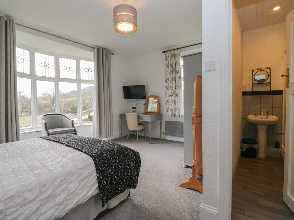 A bedroom with a bed, desk, chair, and a bathroom at Herdwick Croft in Bassenthwaite