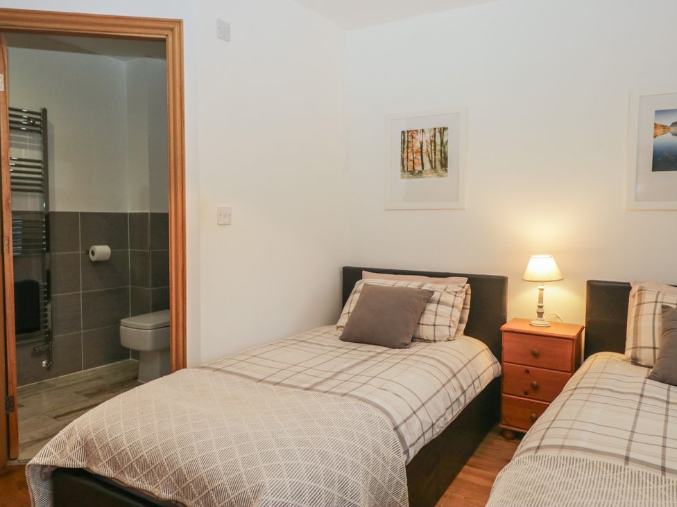 A bedroom with two beds and a bathroom door at Newlands Cottage in Keswick