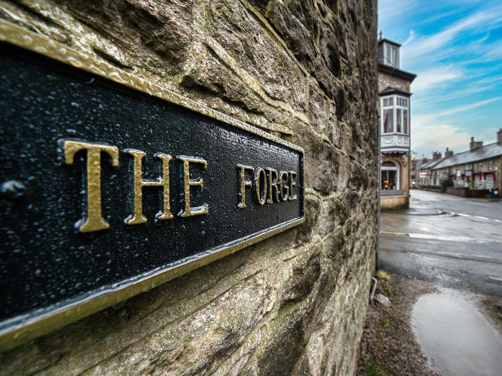 A sign for The Forge next to a stone wall in Castleton, Peak District