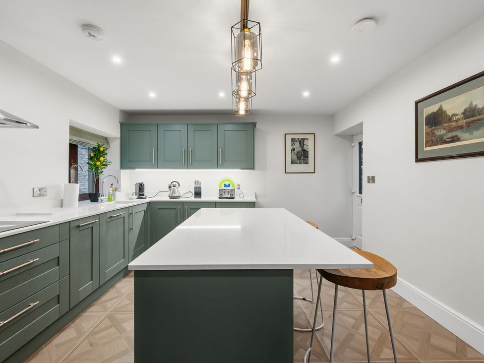 A kitchen with green cabinets and a white island at The Forge in Castleton, Peak District