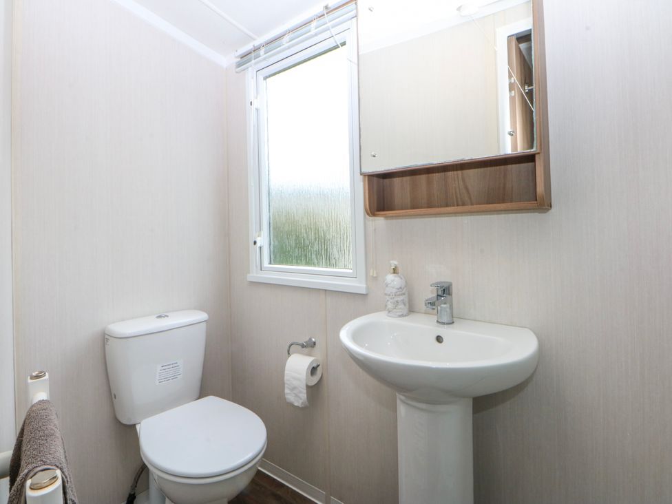 A bathroom with a toilet, sink, and window at 49 Cader Idris, Hafan-Y-Mor Holiday Park in Pwllheli