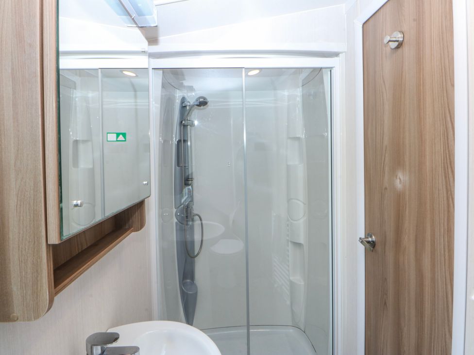 A bathroom with a shower, sink, and mirror at 49 Cader Idris, Hafan-Y-Mor Holiday Park in Pwllheli