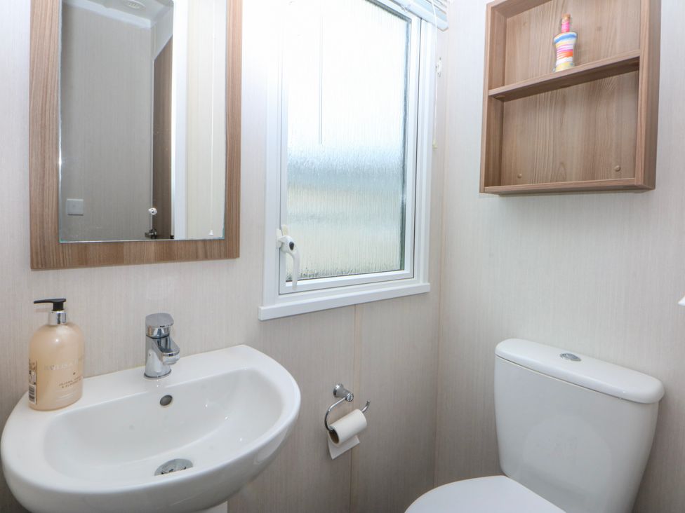 A bathroom with a sink, toilet, and a window at 49 Cader Idris, Hafan-Y-Mor Holiday Park Pwllheli