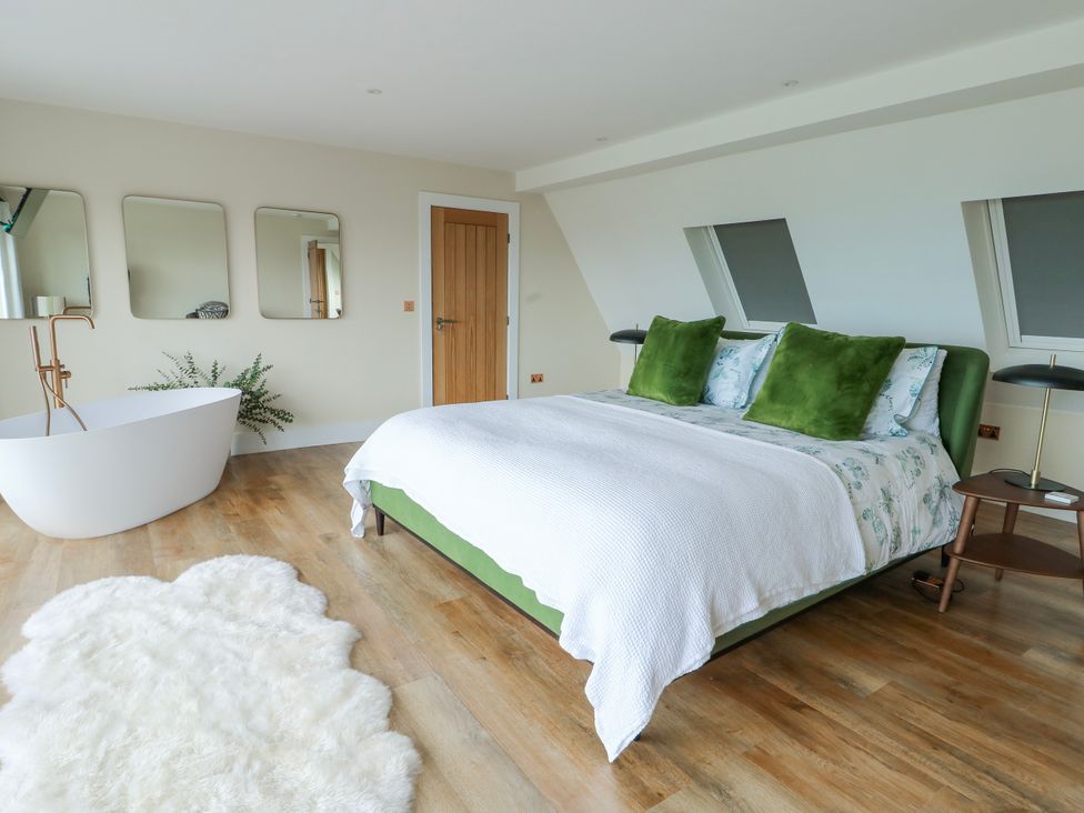 A bedroom with a bed, bathtub, and mirrors at Pengarnedd in Amlwch