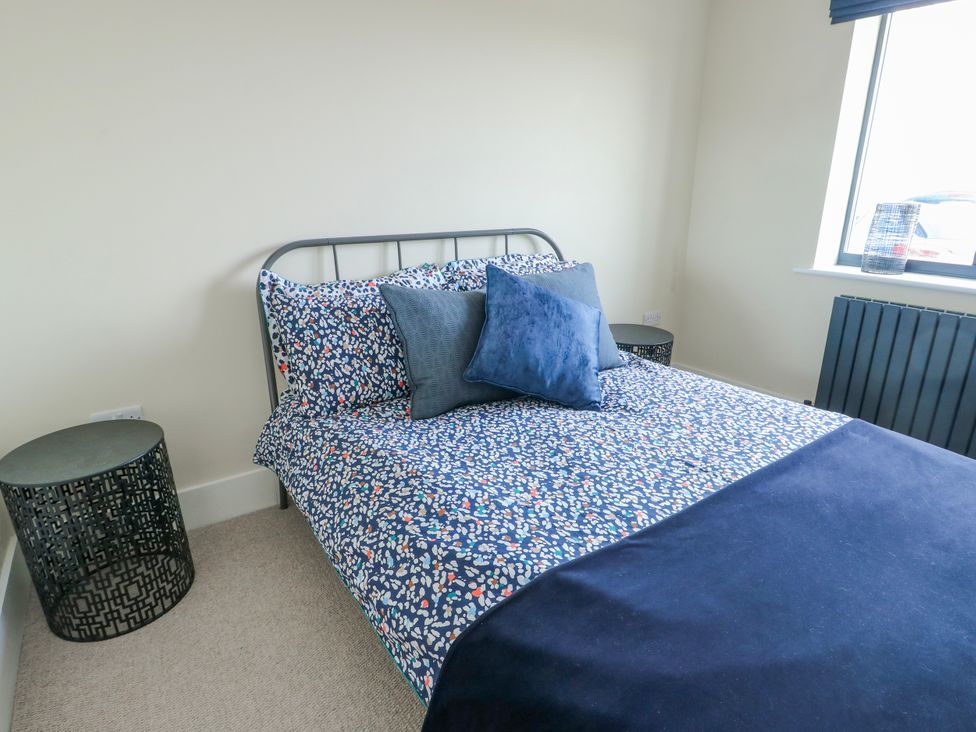 A bedroom with a bed, cushions, bedside table, and a window at Pengarnedd in Amlwch