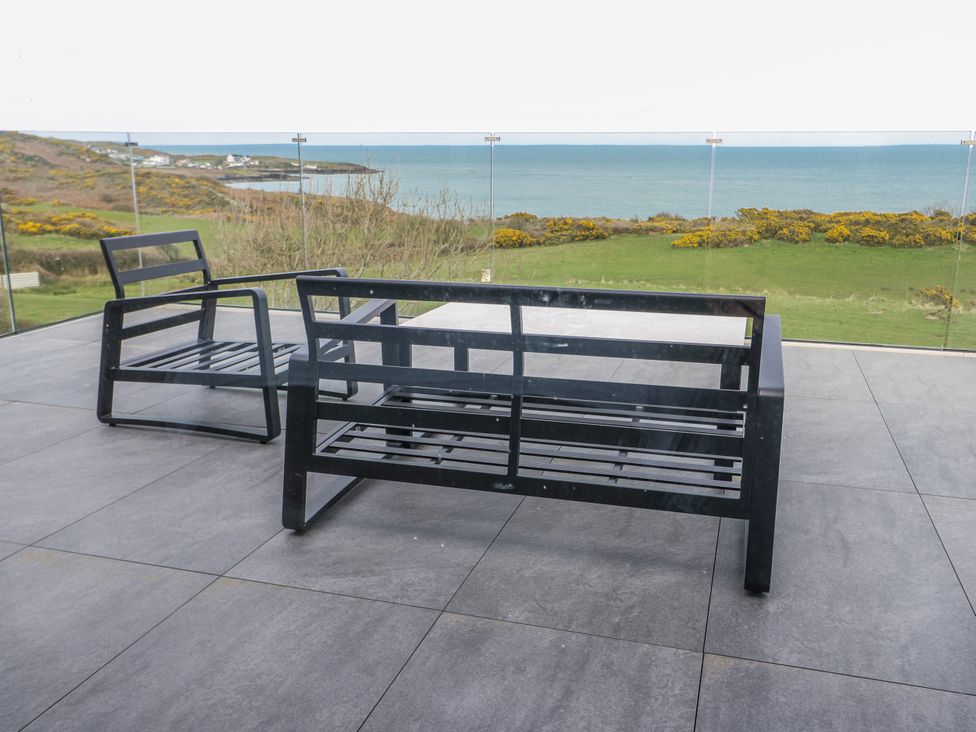 A patio with chairs and a table overlooking the sea at Pengarnedd Amlwch