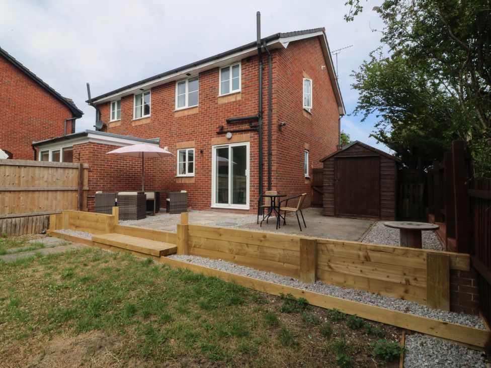 A garden with a patio, table, chairs, and shed at Meadow View in Kinmel Bay