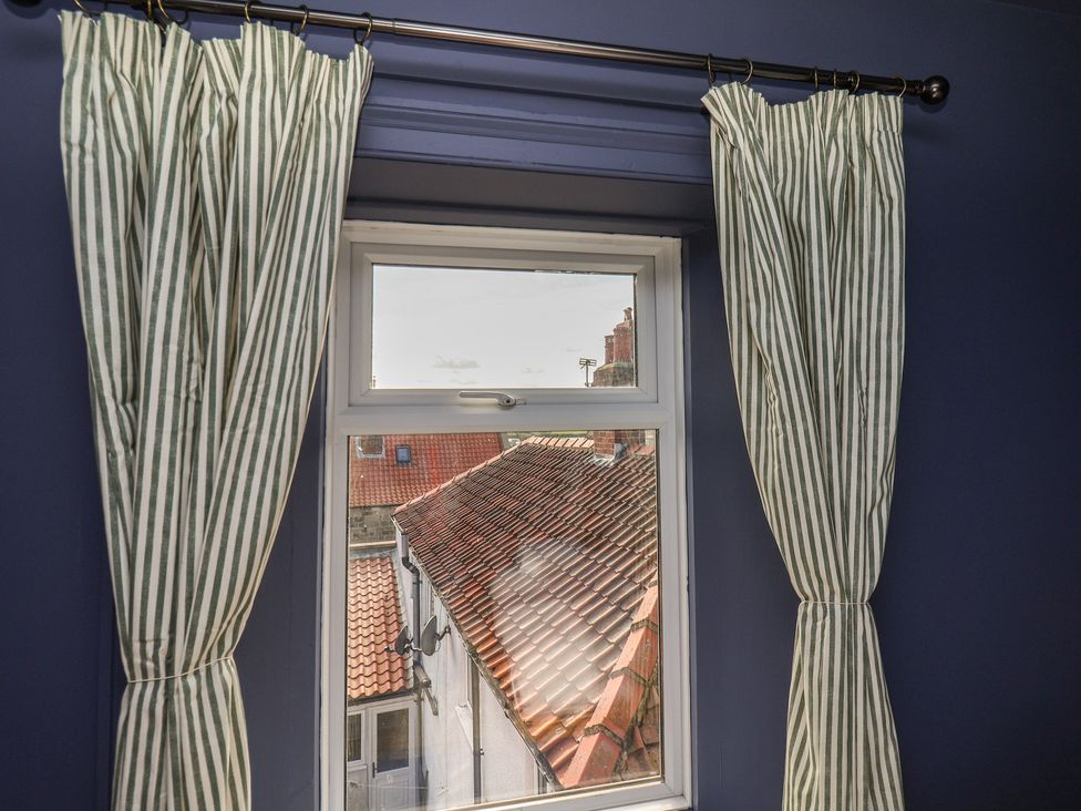 A window with striped curtains showing rooftops at Mulgrave House in Hinderwell near Staithes