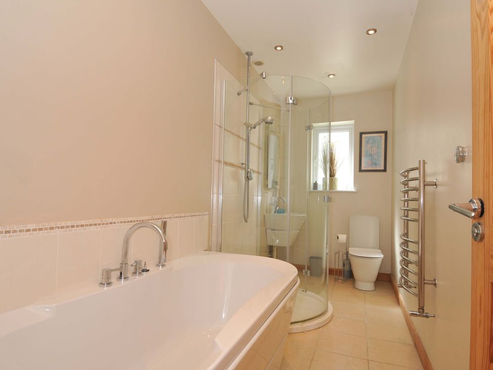 A bathroom with a bath tub, shower, toilet, and sink at Porthmeor in Wadebridge