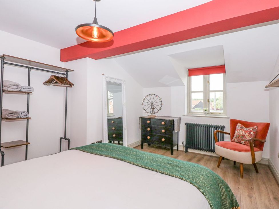 A bedroom with a bed, wardrobe, and chair at Joy's Cottage Snettisham