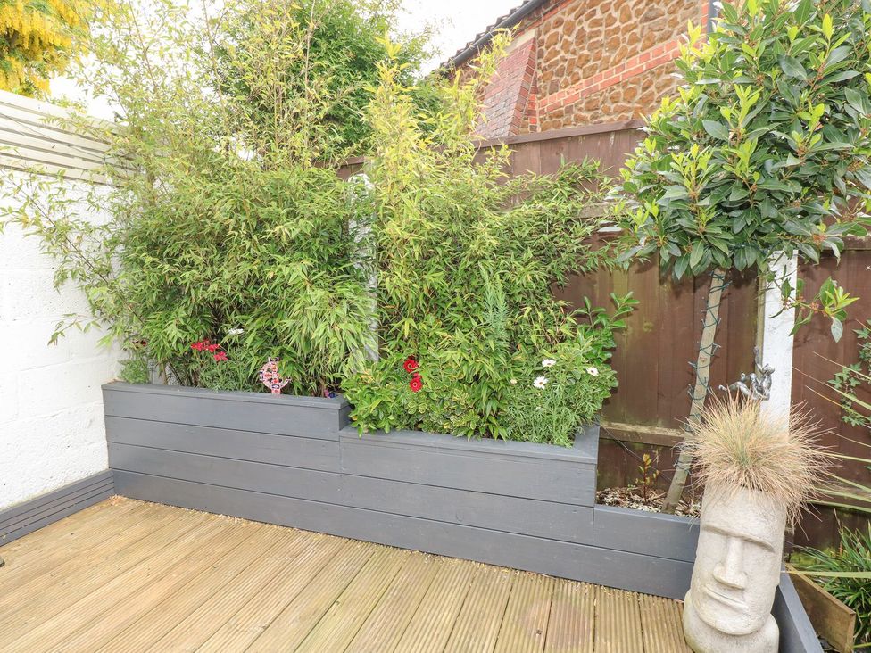 A garden with potted plants and wooden decking at Joy's Cottage in Snettisham