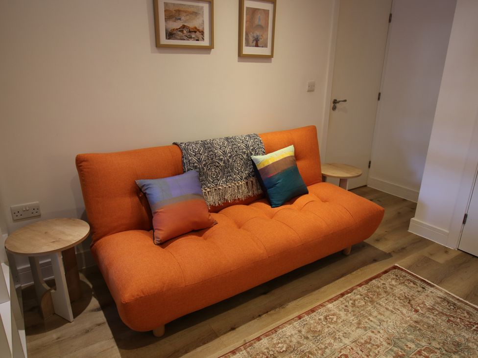 A living room with an orange sofa and side tables at 11 Fountain Court in Falmouth