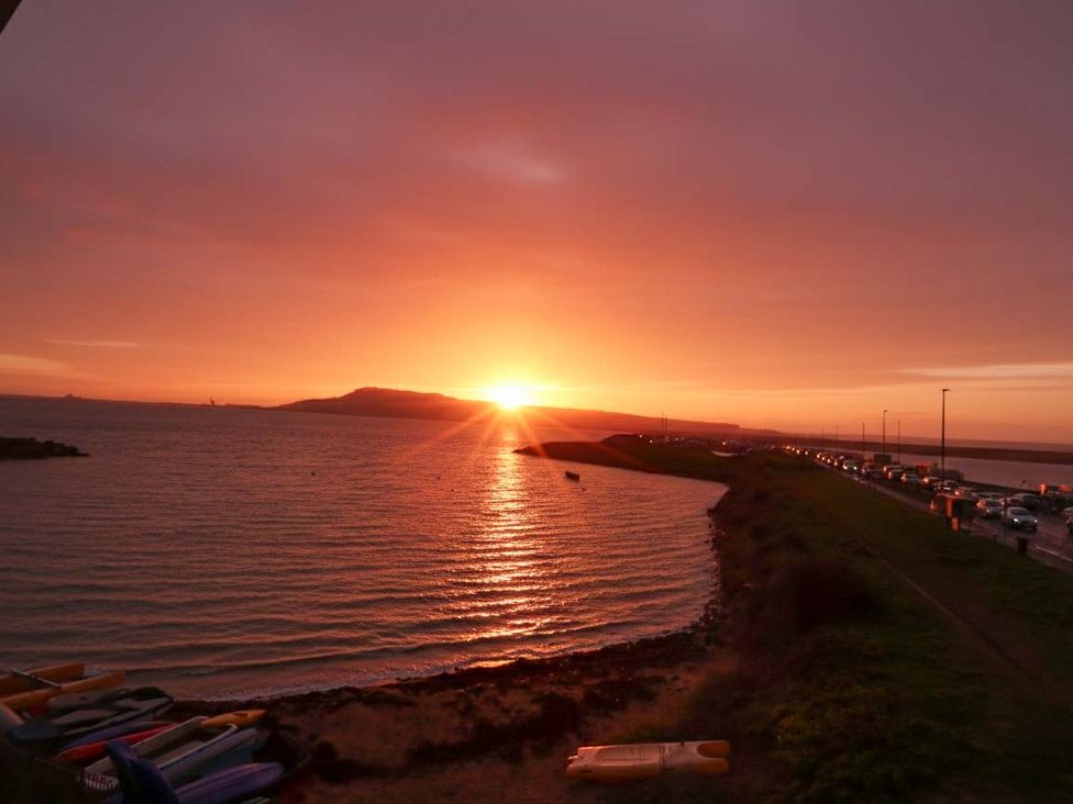 A sunset over the ocean with a road and vehicles at Still Waters in Weymouth