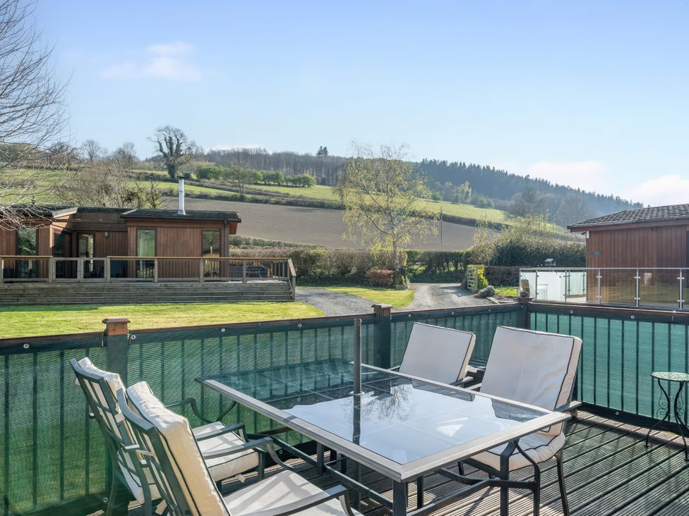 A terrace with chairs and a table overlooking hills at Hazel Lodge in Craven Arms