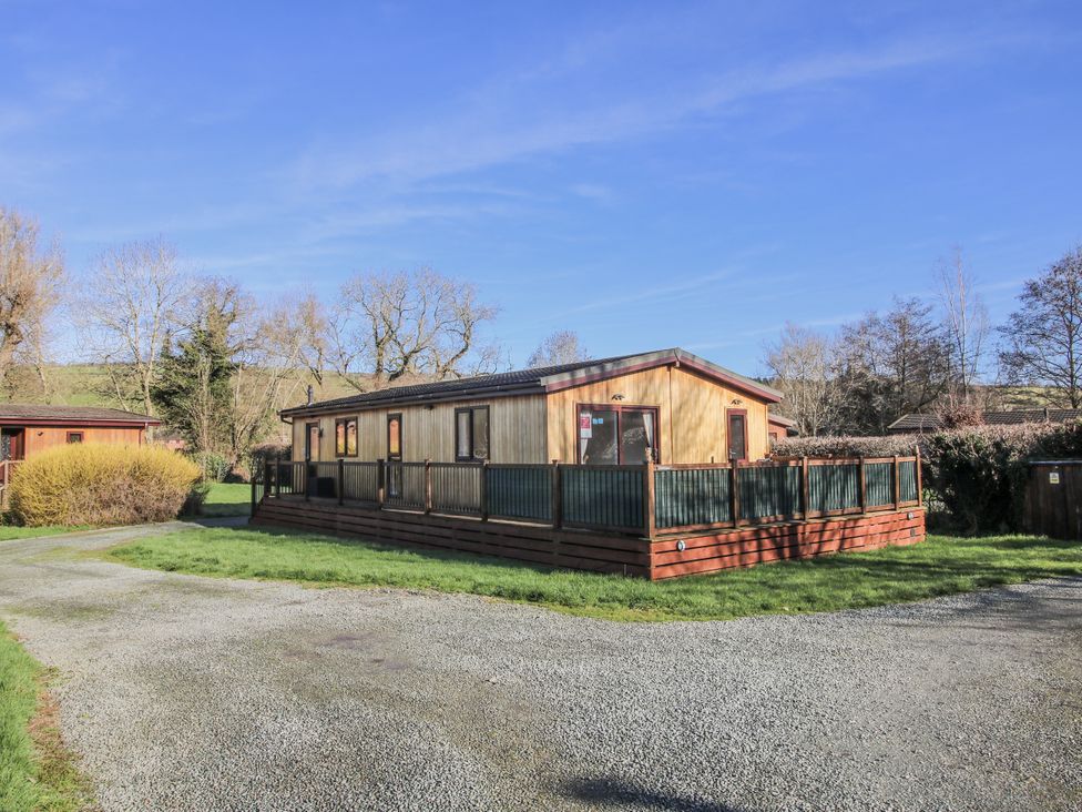 A wooden lodge with a fence and gravel driveway at Hazel Lodge in Clunton near Clun