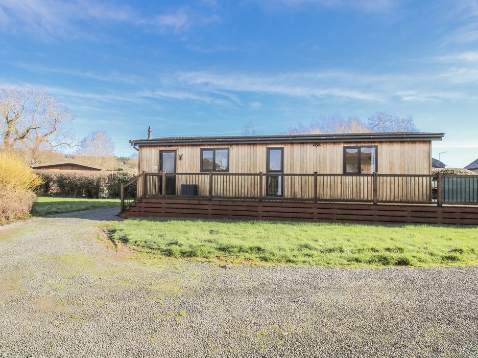 A wooden cabin with a deck and gravel path at Hazel Lodge Clunton near Clun