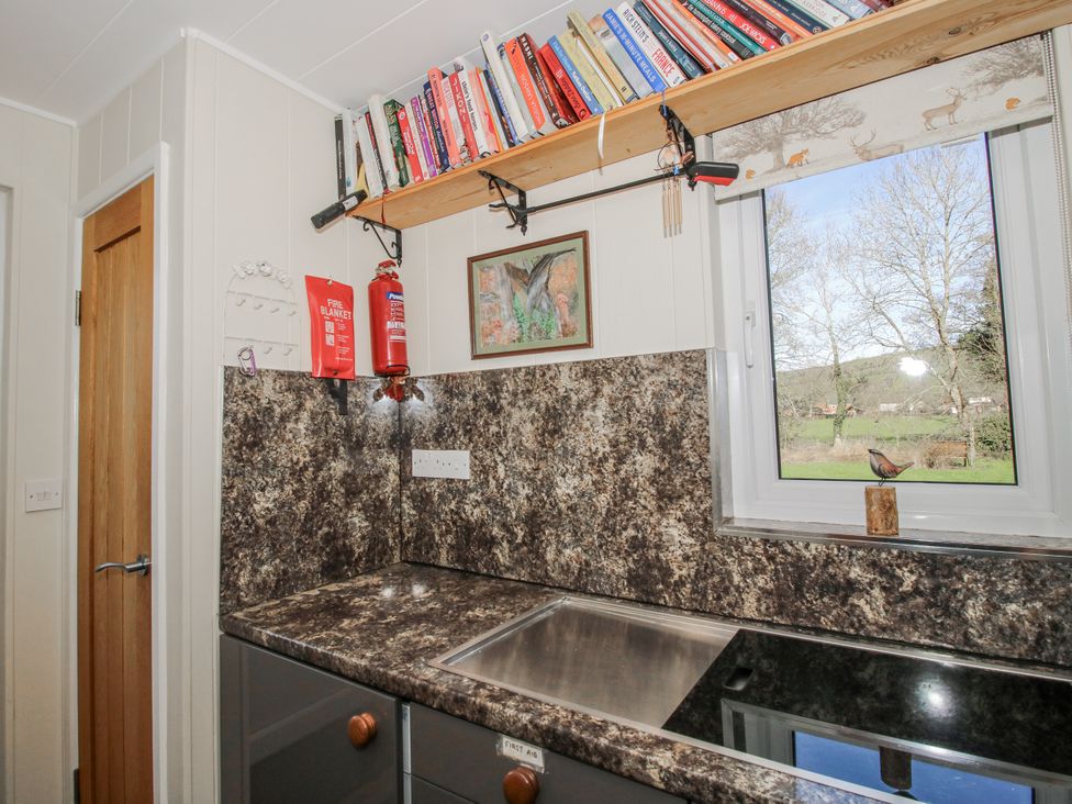 A kitchen with a sink and shelf containing books at Hazel Lodge in Clunton near Clun