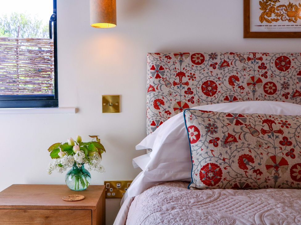 A bedroom with a bed, headboard, lamp, vase, and flowers at The Barn