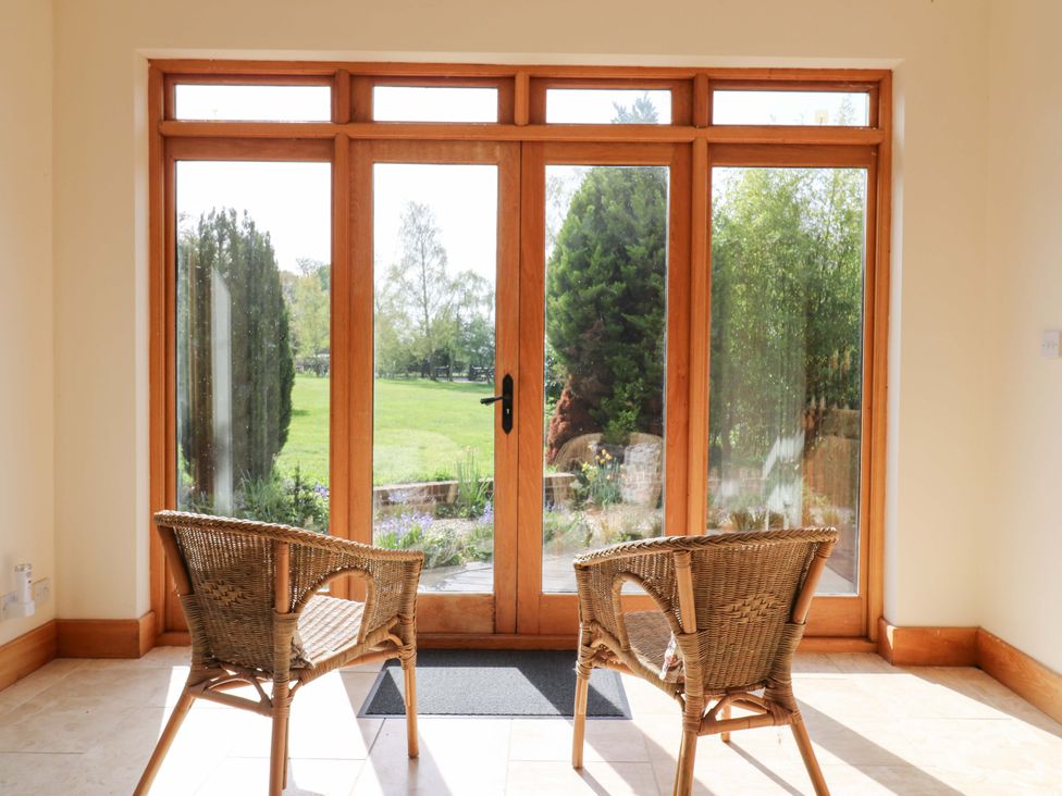 A conservatory with wicker chairs and double doors leading to a garden at Six Apples in Wethersfield near Finchingfield
