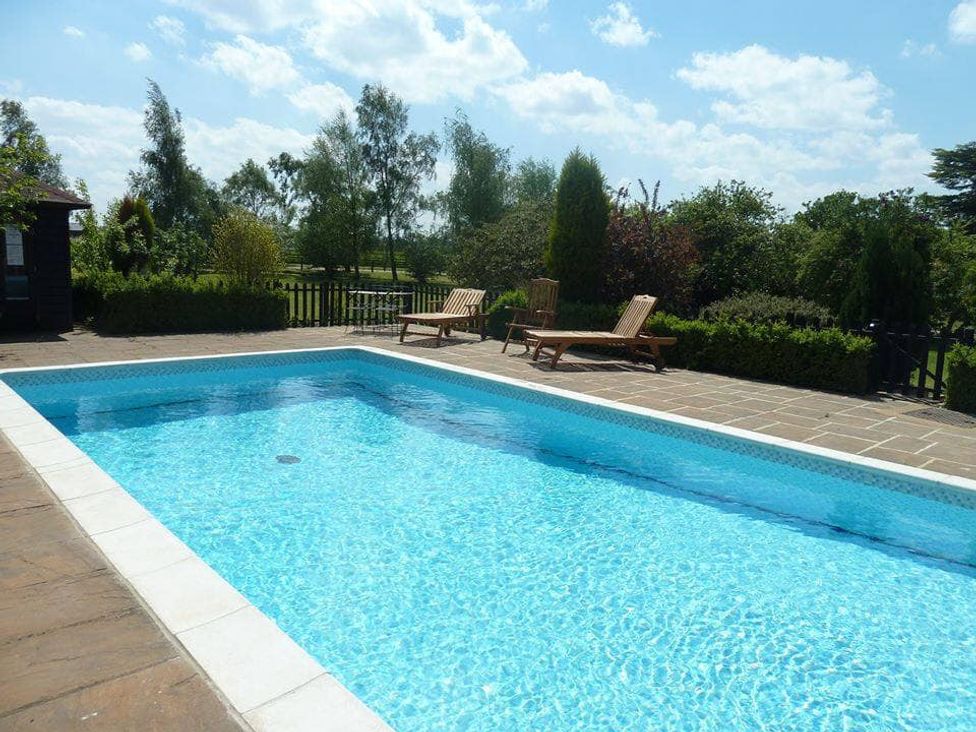 A swimming pool with deck chairs and a garden at Six Apples Wethersfield near Finchingfield