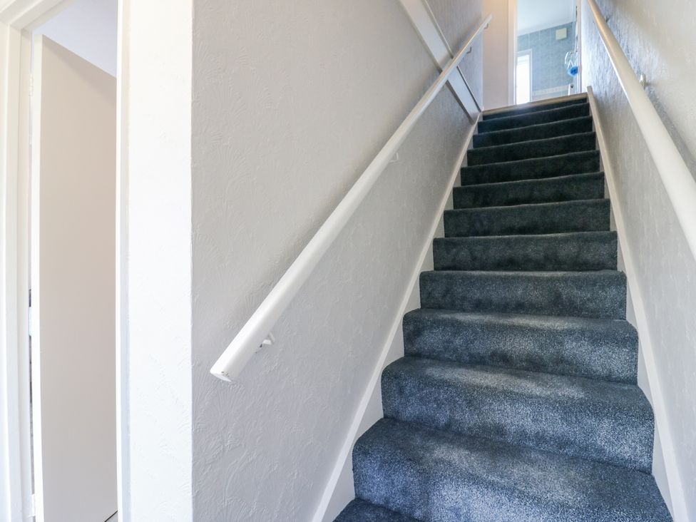 A staircase with grey carpet and a handrail at Sea Rose Cottage